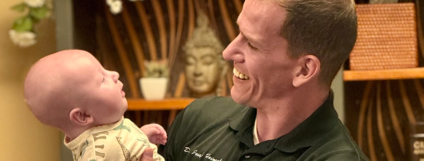 Why Kids and Infants Need Chiropractic Too featuring Dr Joe holding a happy infant