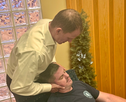 Dr. Joe Heinecke, DC performing a seated cervical adjustment on a male patient.
