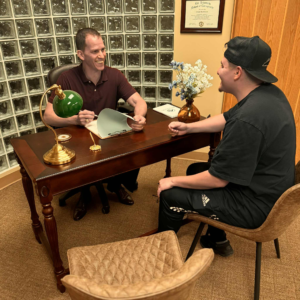 Dr. Joe Heinecke, DC and male patient sitting at his desk consulting during a visit.