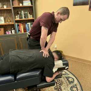 Dr. Joe Heinecke, DC is adjusting a male patient's upper back.