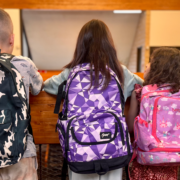Three children wearing their colorful backpacks overlooking a balcony.