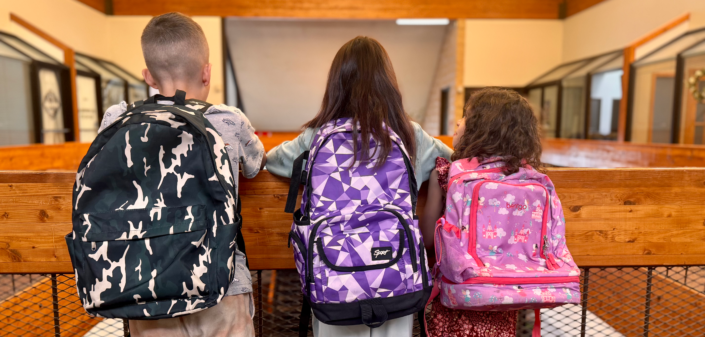 Three children wearing their colorful backpacks overlooking a balcony.