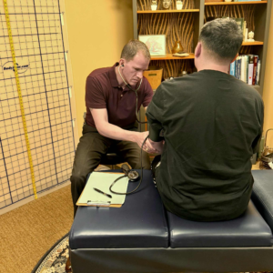 Dr. Joe Heinecke, DC is checking a male patient's blood pressure during an annual examination.