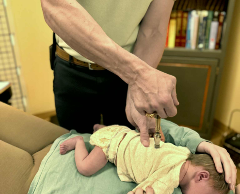 Dr. Joe Heinecke, D.C. is using an activator instrument to adjust a newborn.