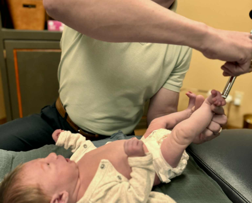 Dr. Joe Heinecke, D.C. is adjusting a newborn's foot with an activator.